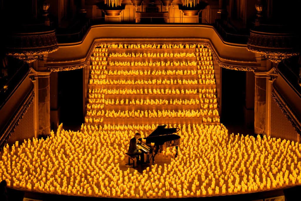 Concert Candlelight au Victoria hall au piano. Un homme joue entouré de centaines de bougies. le théâtre est rempli d'ornements et de décoration. Les bougies éclairent la salle de concert