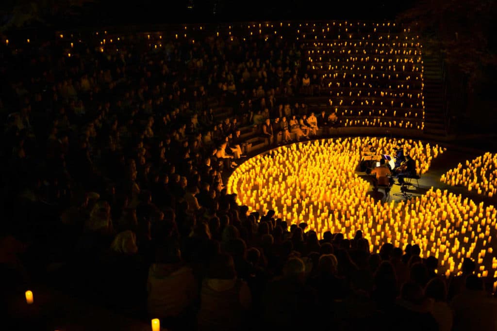 Concert Candlelight à Genève au théâtre grec. le pianiste est face au public assis sur l'estrade de l'amphithéâtre disposé en cercle autour du piano et des bougies.