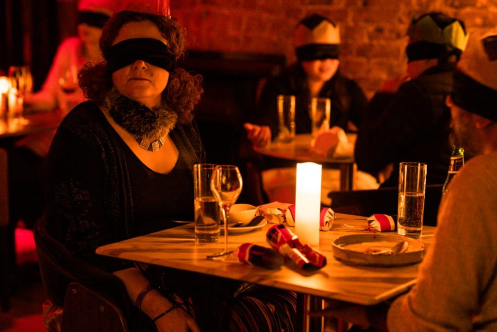 Dining in the dark : diner à l'aveugle entre deux personnes dont une femme face à la caméra les yeux bandés