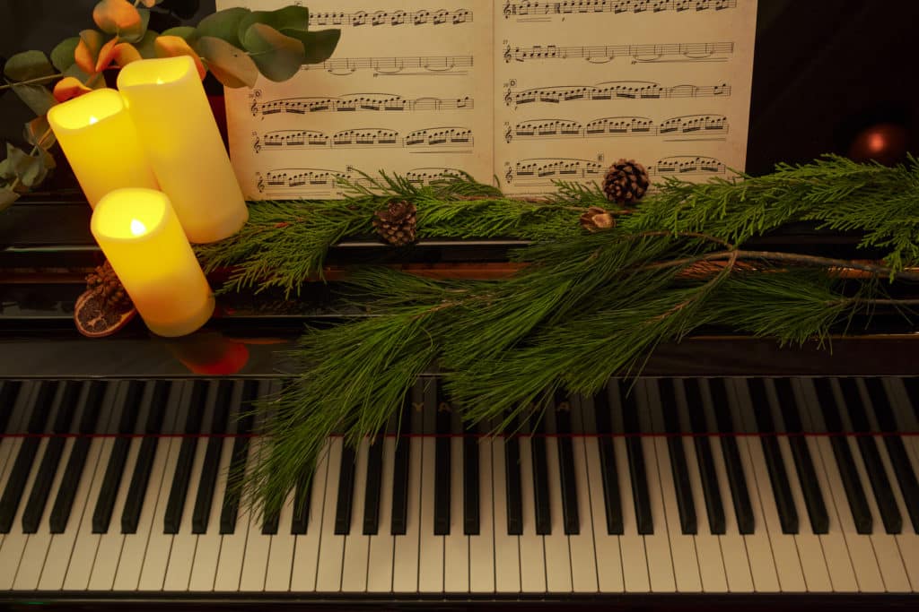 Photo d'un piano en gros plan décoré avec des branches de sapin et des bougies pour un concert Candlelight spécial Noël